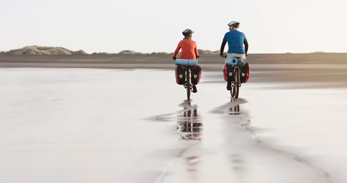 Couple riding bikes with saddlebags on deserted beach