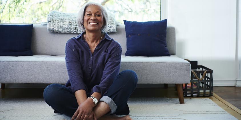 Retiree sitting cross legged on floor in front of grey couch