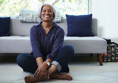 Retiree sitting cross legged on floor in front of grey couch