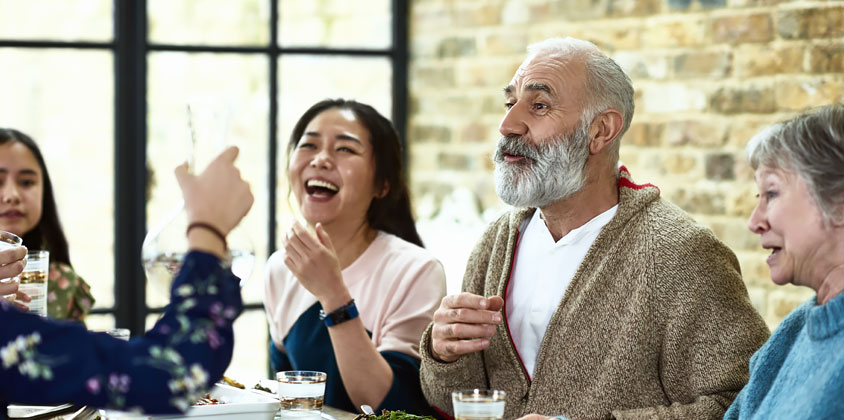 Elderly man with grey beard sitting at table with family members