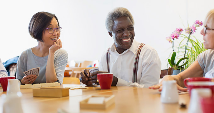 Elderly man and two older ladies sitting at table playing cards