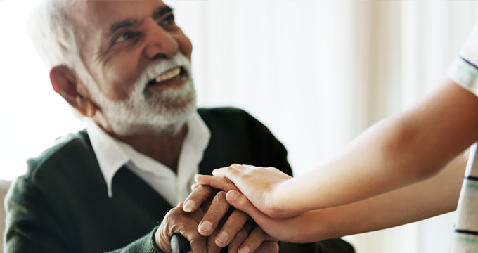 Elderly man with beard sitting while holding hands with a younger person