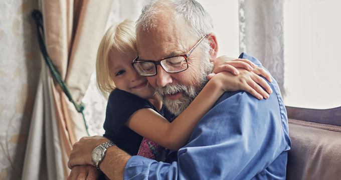 Elderly man wearing blue shirt and glasses hugging his grand child