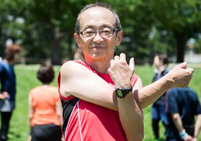 Elderly man with glasses in red singlet stretching for exercise