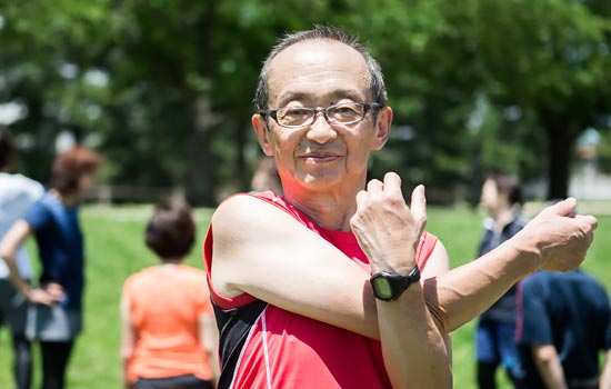 Elderly man with glasses in red singlet stretching for exercise