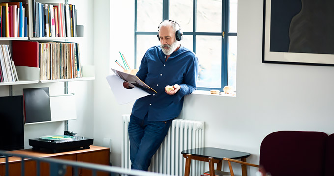 Elderly man with grey beard listening to music with headphones in living room
