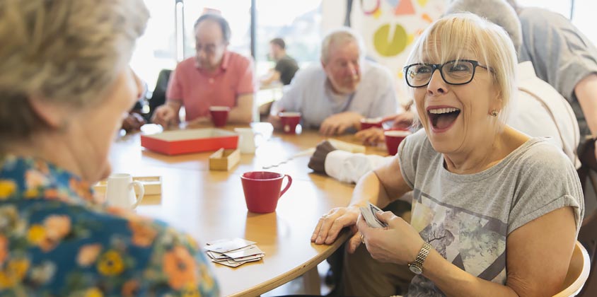 Group of retirees sitting at table playing cards and laughing