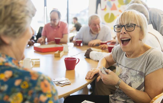 Group of retirees sitting at table playing cards and laughing