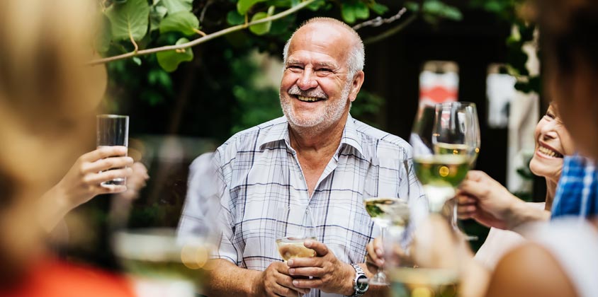 Group of friends holiding wine glasses toasting older gentleman