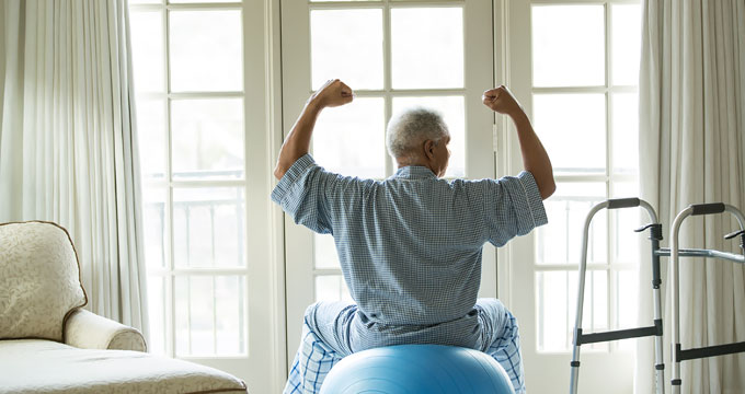 Older man flexing his muscles while sitting on an exercise ball